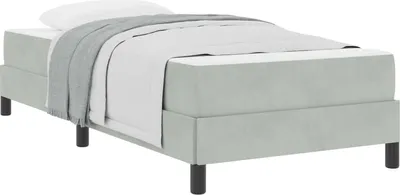 A light gray boxspring bed with a mattress, white sheets, and a gray blanket is shown from a side angle.
