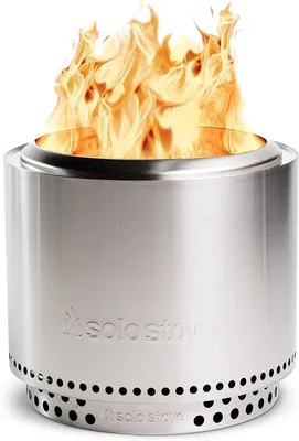 A stainless steel Solo Stove Bonfire with flames burning inside, shown from a slightly low angle.