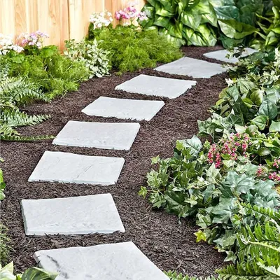 A garden path made of stepping stones surrounded by plants and mulch.