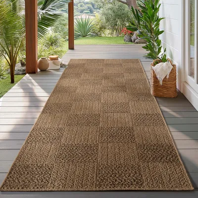 A long, brown rug with a textured pattern is laid out on a wooden deck, surrounded by lush greenery and plants.