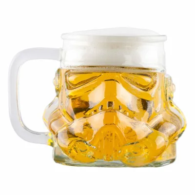 A glass beer mug shaped like a Stormtrooper helmet, filled with beer and foam, isolated on a white background.