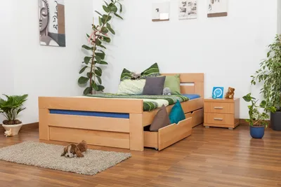 A bedroom scene featuring a wooden bed with drawers, bedding, pillows, and surrounding decor.
