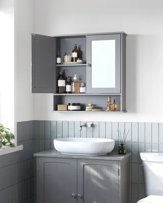 A gray bathroom cabinet with a mirror and open doors, displaying various toiletries. Below the cabinet is a white sink on a gray vanity. The wall is tiled with light blue vertical tiles.