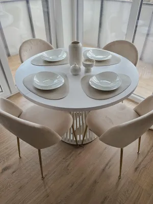 A round white dining table with four beige chairs and placemats with bowls set for a meal.
