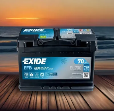 A car battery is displayed on a wooden surface with a beach and sunset in the background.