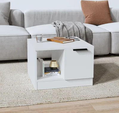 A white coffee table with books and a glass of water on top, placed on a rug in front of a couch.
