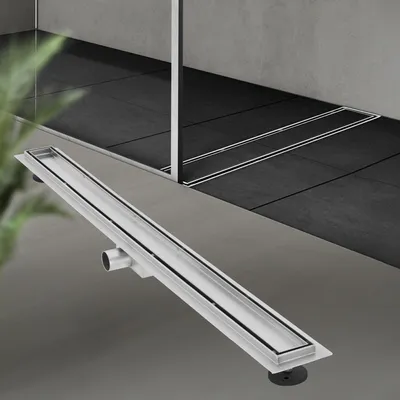 A linear shower drain is shown in the foreground, with a tiled shower area in the background.