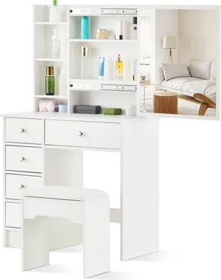 A white vanity table with drawers and shelves, accompanied by a matching stool, set against a white background. A reflection in the mirror shows a bedroom scene.