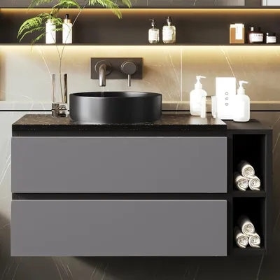 A modern bathroom vanity with a black sink and gray drawers, featuring rolled towels in open shelving.