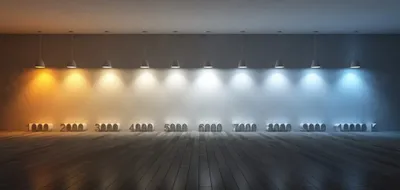 A room with multiple pendant lights hanging from the ceiling, each emitting a different color temperature of light. The lights range from warm orange to cool blue, with numerical labels indicating Kelvin temperatures below each light source.