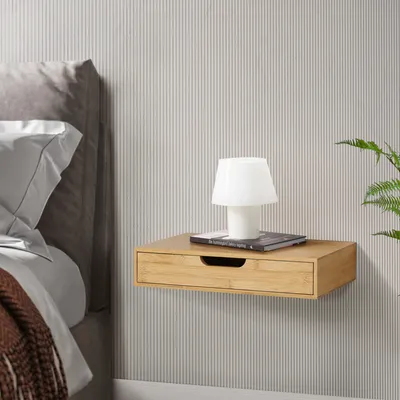 A floating nightstand with a drawer, a book, and a lamp next to a bed.