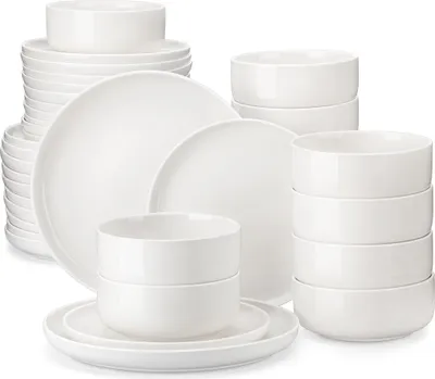 A collection of white ceramic plates and bowls are stacked and arranged on a white background.