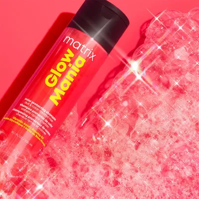 A bottle of Matrix Glow Mania shampoo is shown with pink foam and sparkling effects.