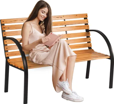 A woman is sitting on a wooden park bench and reading a book.