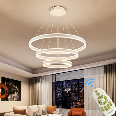 A modern living room with a sofa, artwork, and a view of a city at night through a large window, featuring a multi-ring LED pendant light.
