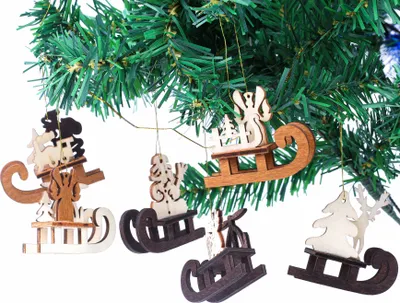 Christmas tree ornaments in the shape of wooden sleds with various figures on them, hanging from a Christmas tree branch.