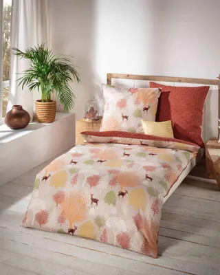 A bed with bedding featuring a forest and deer pattern, set in a room with a window and plants.