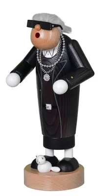A wooden figurine of a person dressed in a suit, wearing sunglasses and jewelry, standing on a wooden base with a small white cat.
