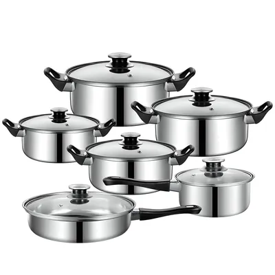 A set of stainless steel pots and pans with glass lids, arranged in a studio setting against a white background.