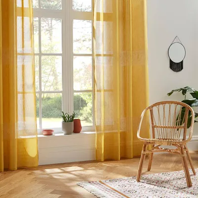 A room with yellow curtains, a wicker chair, and a window overlooking greenery.
