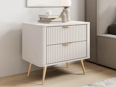 A beige nightstand with gold legs and handles, placed next to a bed.