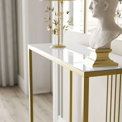 A close-up shot of a console table with a white glass top and gold metal frame, placed in a well-lit room with curtains and a bust on top.