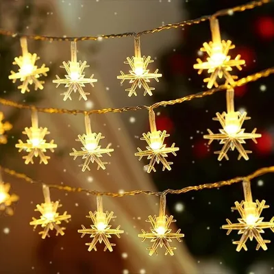 A string of snowflake-shaped lights is draped across a dark, festive background, with soft bokeh lights and falling snow effects.