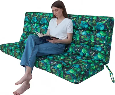 A woman is sitting on a large, green, leaf-patterned cushion, reading a book.