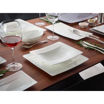 A table setting with white dinnerware, wine glasses, and cutlery.
