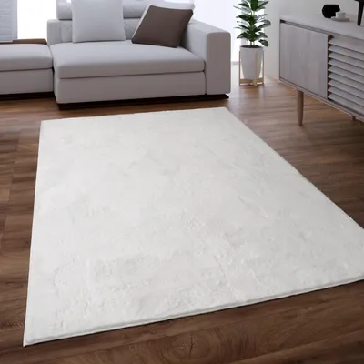 A white shaggy rug is placed on a wooden floor in front of a modern sofa and a cabinet.