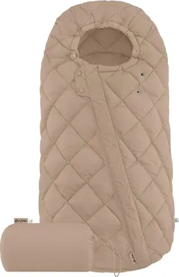 A beige quilted footmuff for a baby, shown lying flat with a small rolled-up bag next to it.