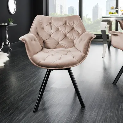 A modern beige velvet armchair with black metal legs is shown in a well-lit room with a dark floor and a window overlooking a city skyline.