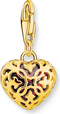 A gold heart-shaped charm with intricate filigree and a red stone inside, suspended from a clasp.