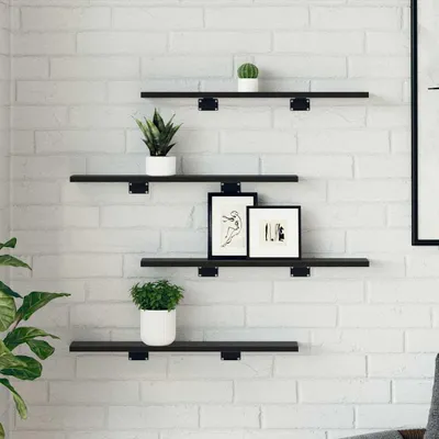 Four black shelves are mounted on a white brick wall, decorated with plants and framed pictures.