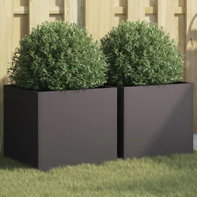 Two square planters with green bushes in them, placed on grass in front of a wooden fence.