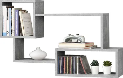 A gray, modern-looking wall shelf with multiple compartments, displaying books, a video game controller, CDs, and decorative plants.