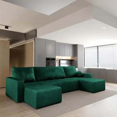 A spacious living room with a large green sectional sofa in the foreground and a modern kitchen area in the background.