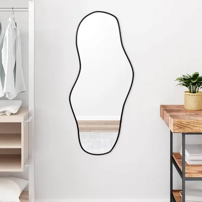 A mirror is hanging on a white wall next to a closet and a wooden table.