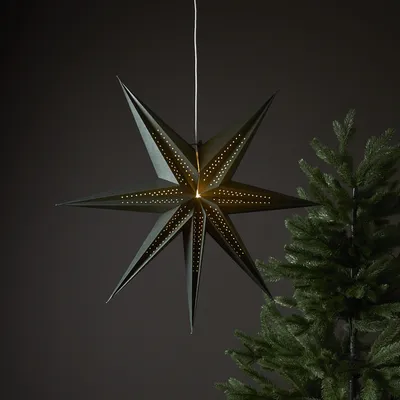 A dark green, seven-pointed star-shaped lantern hangs in front of a dark gray background, with a portion of a green Christmas tree visible on the right.