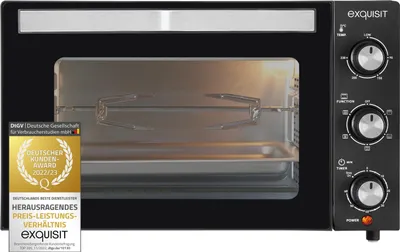 A black mini oven with a rotisserie spit inside, shown from the front. A badge is visible on the left side.