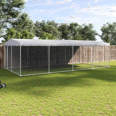 A large outdoor dog kennel with a grey roof, set up on a grassy lawn with trees and a wooden fence in the background.