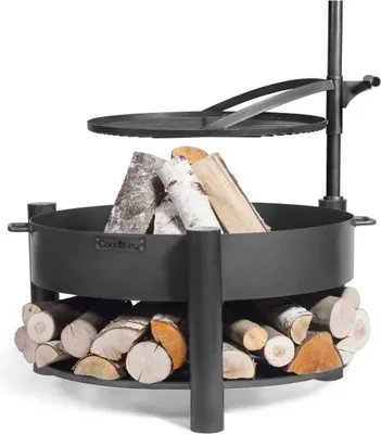 A black metal fire pit with firewood stacked inside and below, with a grill grate suspended above.