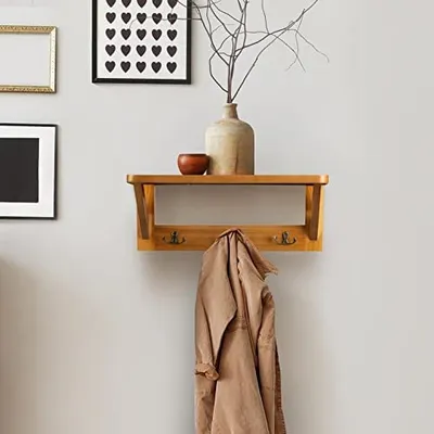 A wooden wall shelf with coat hooks, decorated with a vase and a small bowl, and a coat hanging from one of the hooks.