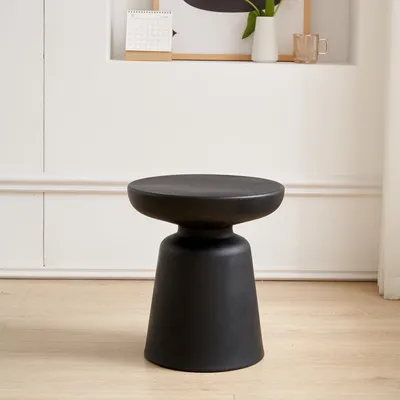 A black side table is shown in a room with white walls and light wood flooring.