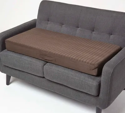 A brown seat cushion is placed on a gray sofa.