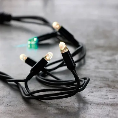 A close-up shot of a string of LED lights with black wires and white and green bulbs, resting on a textured gray surface.