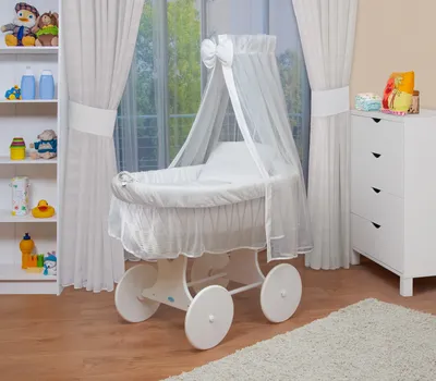 A baby bassinet set is displayed in a nursery setting, next to a white dresser and a bookshelf.