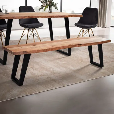 A wooden bench with black metal legs is placed in front of a dining table with chairs, on a rug in a dining room setting.