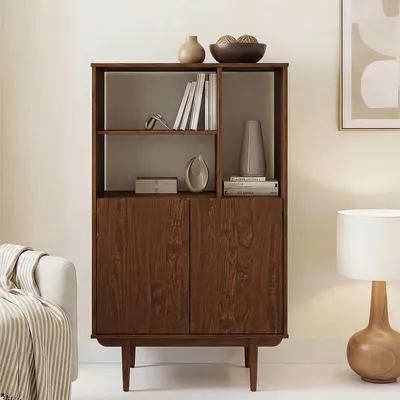 A wooden highboard with open shelves and doors, decorated with vases and books, in a living room setting next to a sofa and a lamp.