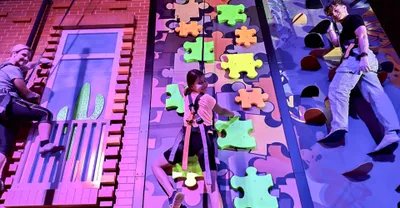 People climbing on a colorful indoor climbing wall with puzzle piece-shaped holds.